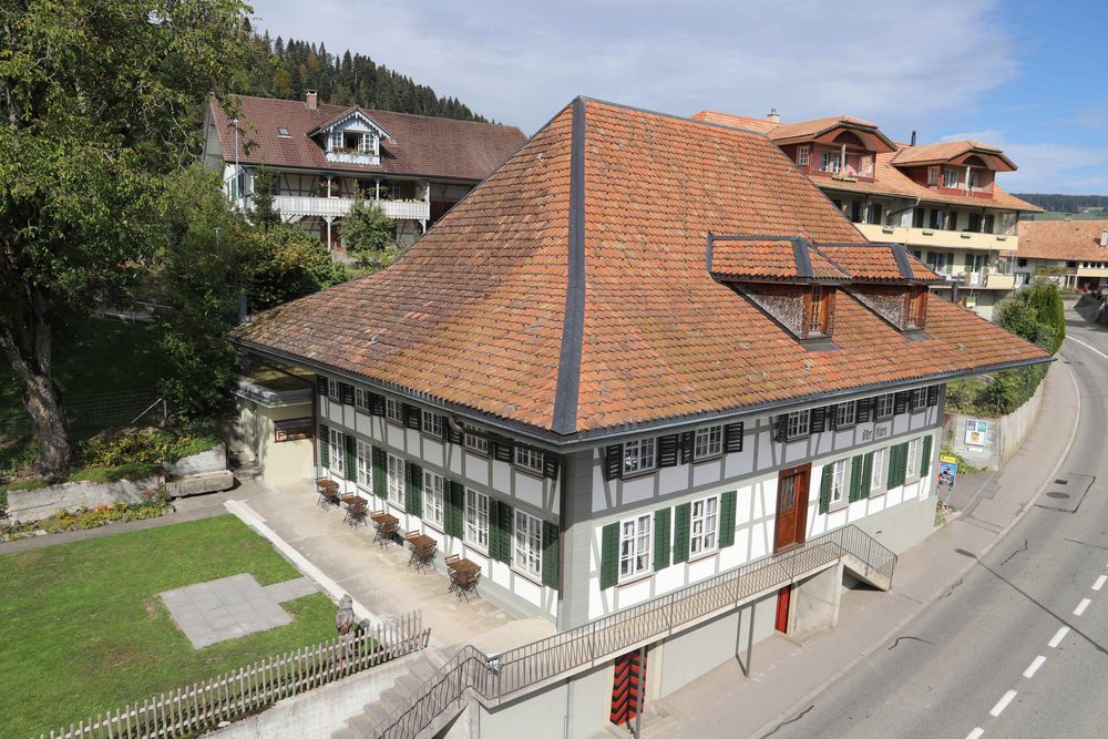 Das historische Gasthaus «Alter Bären» in Konolfingen: heller Riegbau mit grünen Fensterläden und steilem, geknicktem Walmdach an der Burgdorfstrasse.
