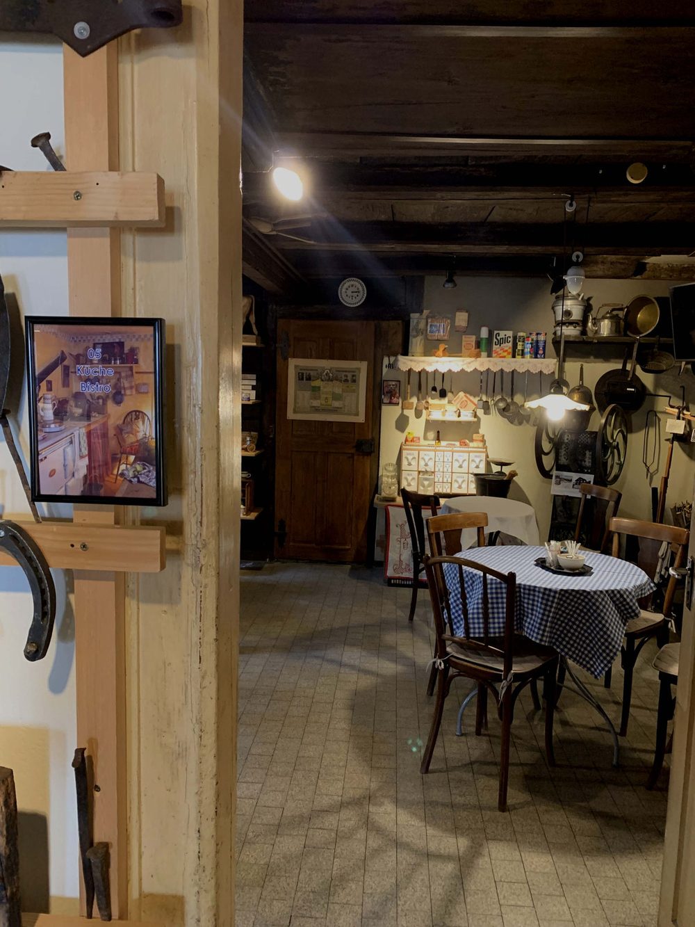 Blick durch die Tür in Küche und Bistro des Dorfmuseums mit gedecktem Tisch und altem Geschirr.