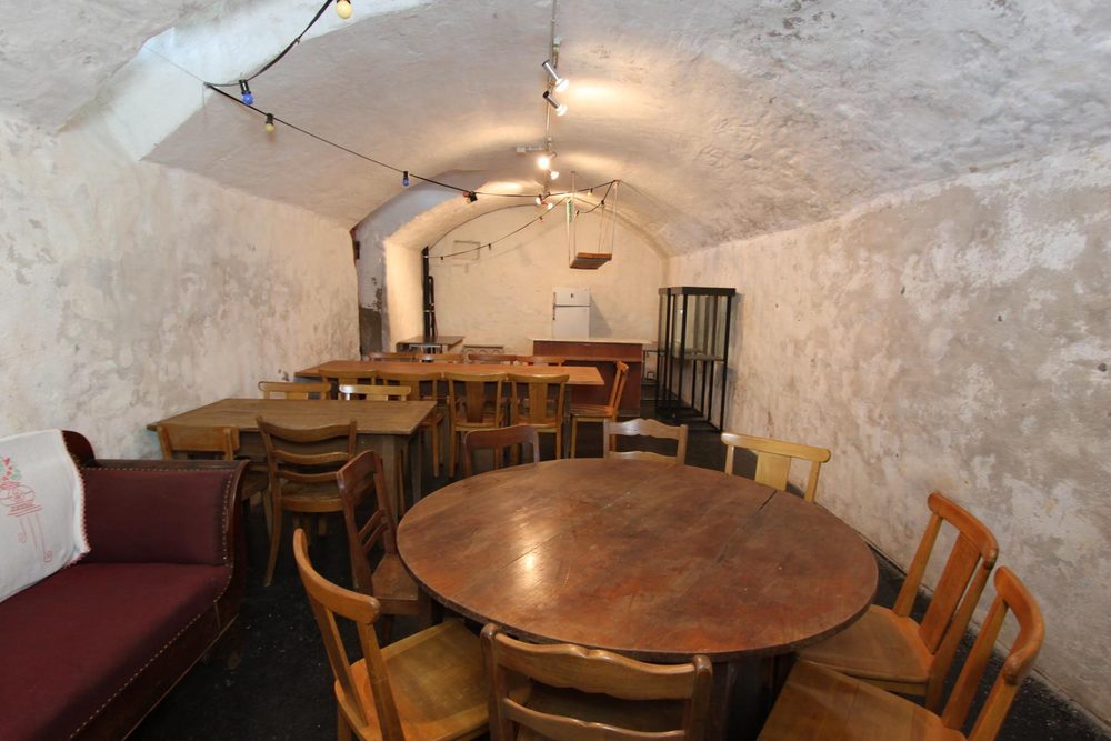 Der gewölbte Keller mit weiss gekalkten Wänden, rundem Tisch und Bank.