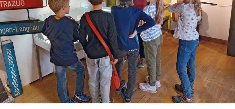 Schulkinder mit Eisenbahner-Mützen stehen vor einer Vitrine im Dorfmuseum.